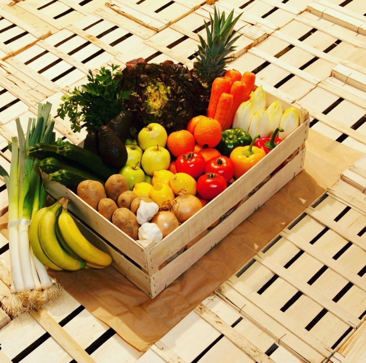 Fruits et légumes frais assortis dans une caisse en bois sur une natte tissée