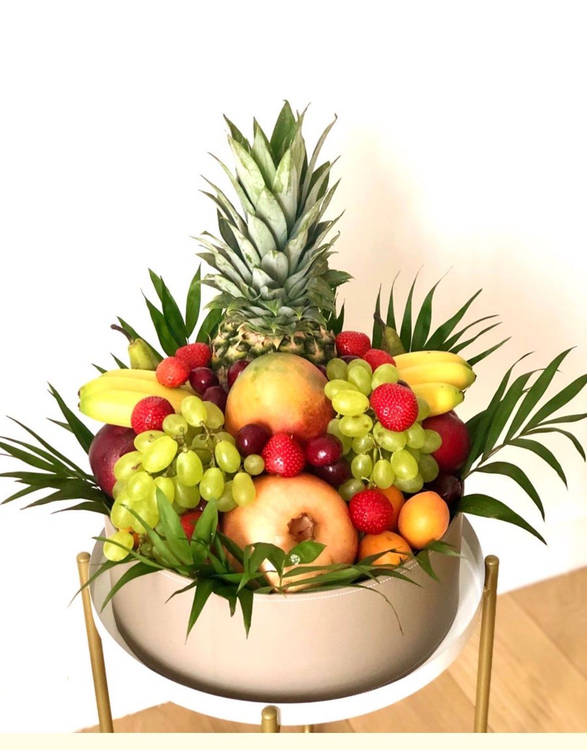 Composition de fruits tropicaux avec ananas, bananes, raisins, pommes et baies dans un bol blanc avec des feuilles