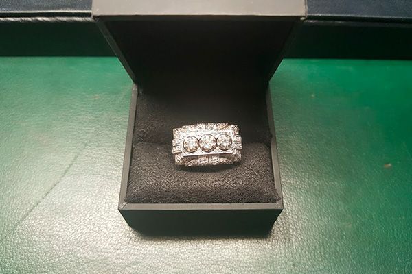Un anillo de diamantes en una caja negra sobre una mesa verde.