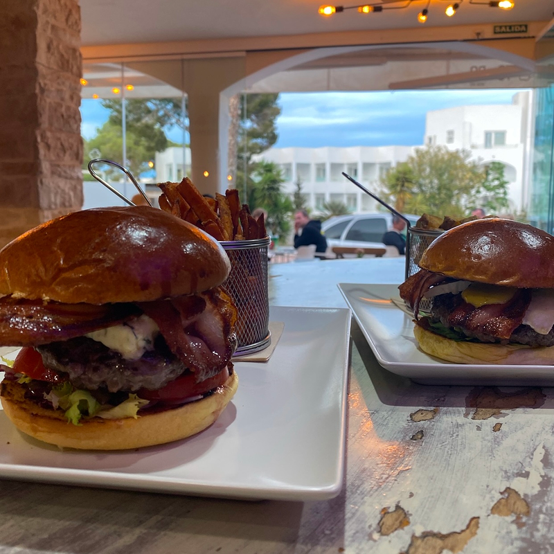 Dos hamburguesas están sentadas en platos blancos sobre una mesa.