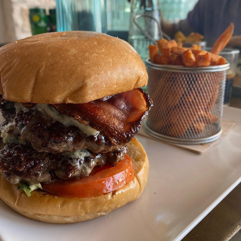 Un primer plano de una hamburguesa en un plato junto a una canasta de papas fritas.