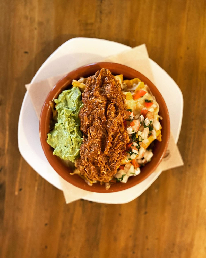 Un tazón de comida con guacamole y carne sobre una mesa de madera.