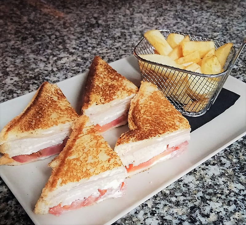 Un plato de sándwiches junto a una canasta de papas fritas