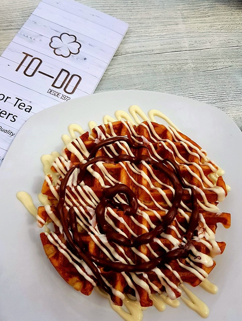 Un gofre con salsa de chocolate y crema batida en un plato junto a una lista de cosas por hacer.