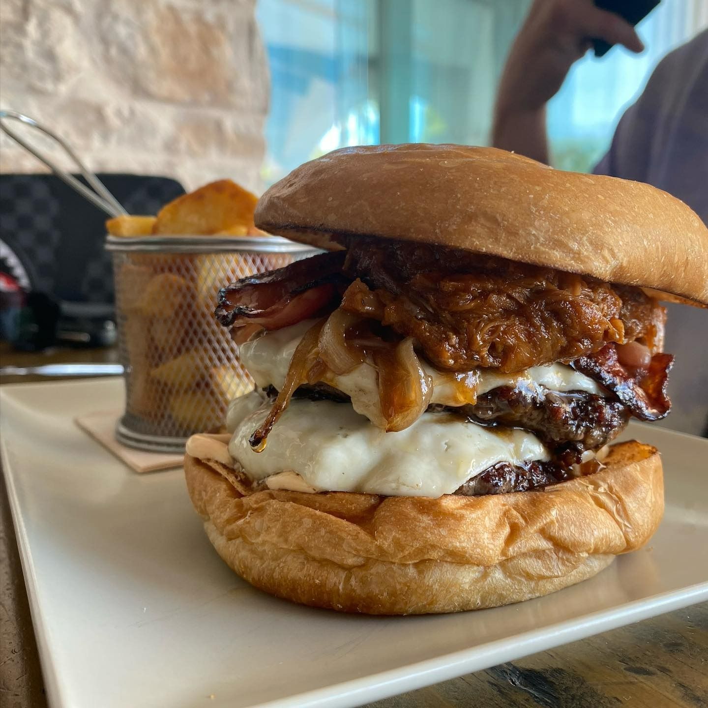 Un primer plano de una hamburguesa en un plato con una canasta de papas fritas en el fondo.