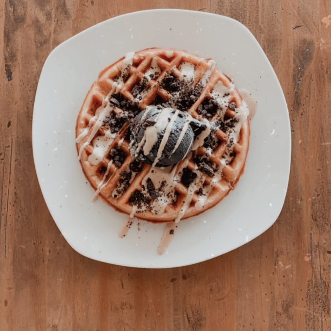 Un plato blanco cubierto con un gofre y helado.