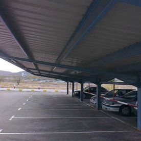 Una fila de coches están aparcados bajo un toldo en un estacionamiento.