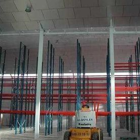 Un hombre conduce un tractor en un gran almacén lleno de estantes.