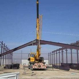 Una grúa está levantando una gran estructura metálica en un sitio de construcción.