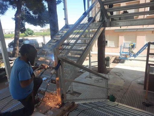 Un hombre está soldando una escalera de metal fuera de un edificio.