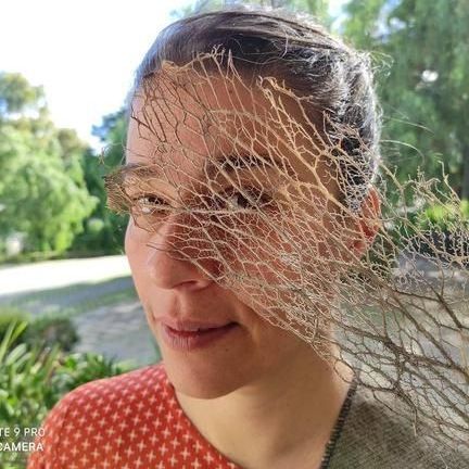 Mujer con una rama seca que le tapa la mitad del rostro al aire libre. Sonríe.