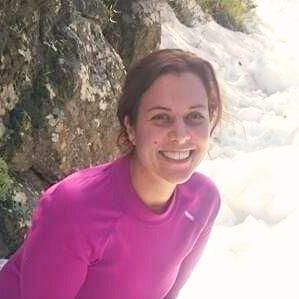 Mujer con camisa rosa sonríe, al aire libre, cerca de una cascada rocosa.