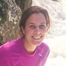 Mujer con camisa rosa sonríe cerca del agua y las rocas.