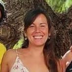 Mujer sonriendo frente a un árbol, vistiendo un top de tirantes finos con estampado floral blanco.