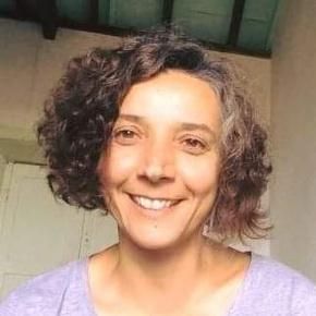 Mujer con cabello oscuro y rizado, sonriente, vistiendo una camisa morada.