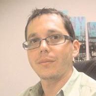 Hombre con gafas mirando a la cámara en un entorno de oficina, vistiendo una camisa verde claro.