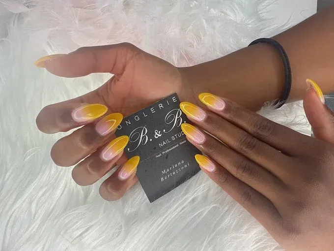 Deux mains présentant des ongles en forme d'amande avec un motif ombré jaune.