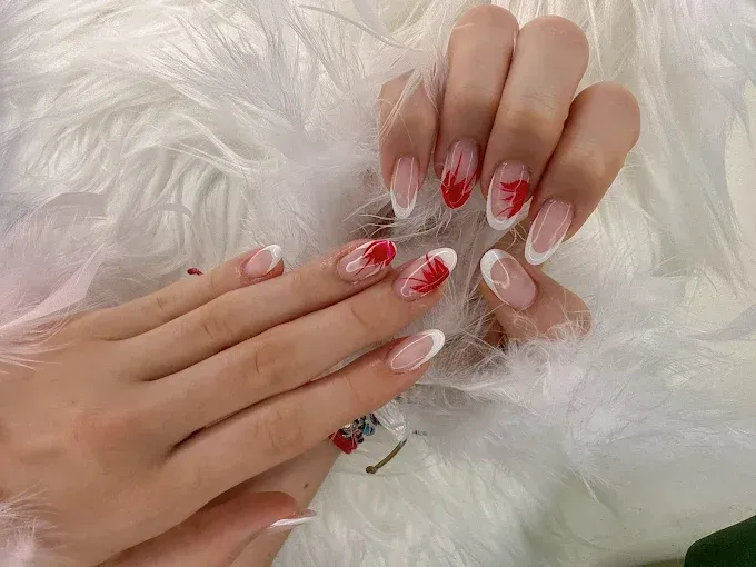 Gros plan sur des ongles en amande ornés d'une manucure française avec des éclaboussures rouges.