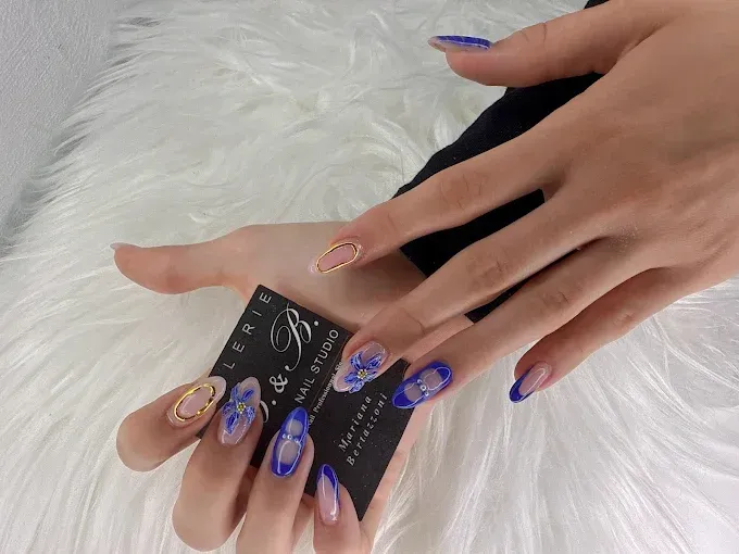 Gros plan sur une main tenant une carte de visite, dévoilant des ongles élaborés en forme d'amande.