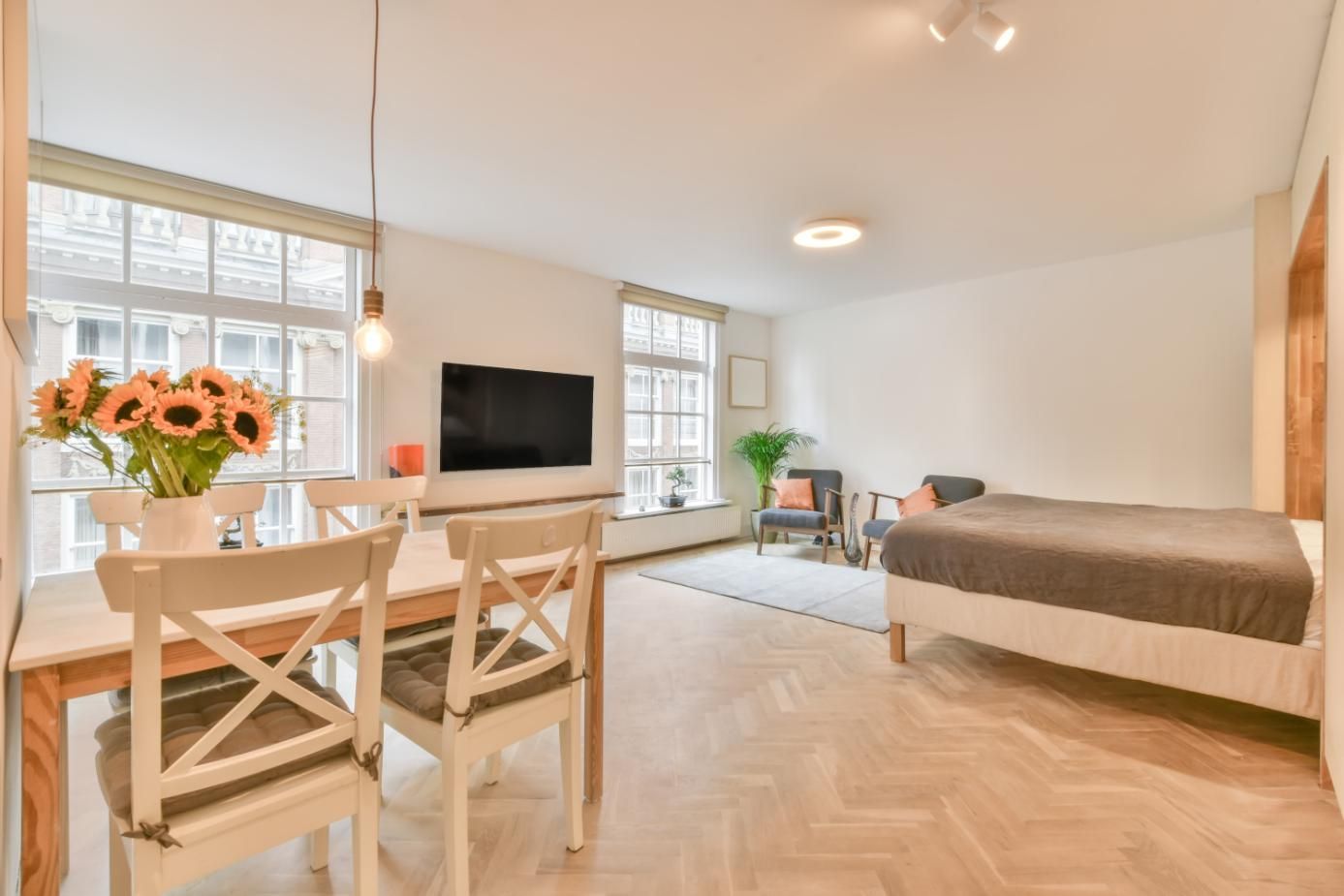 Espacio habitable con mesa de comedor, cama, TV y dos grandes ventanales.