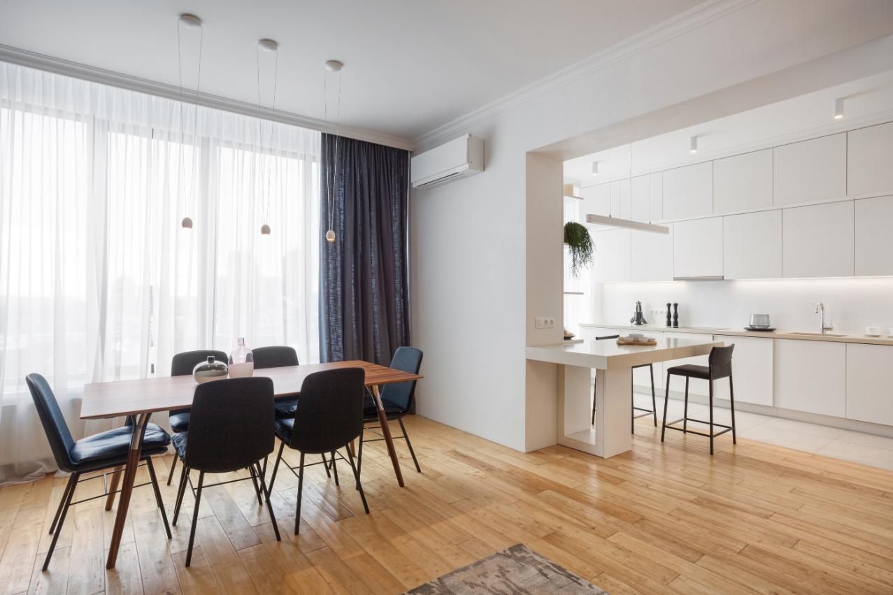 Comedor moderno con mesa y sillas, adyacente a una cocina blanca con barra de desayuno.