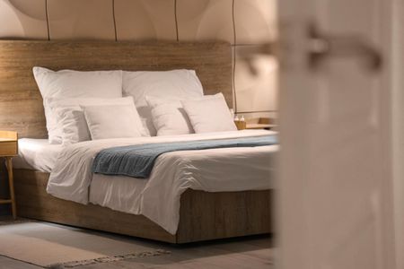 Dormitorio con cabecero de madera, ropa de cama blanca y manta azul.