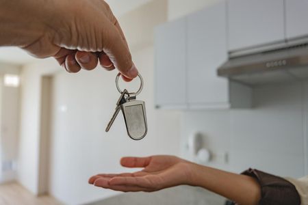 Persona entregando llaves en un llavero a otra persona frente a una cocina blanca.