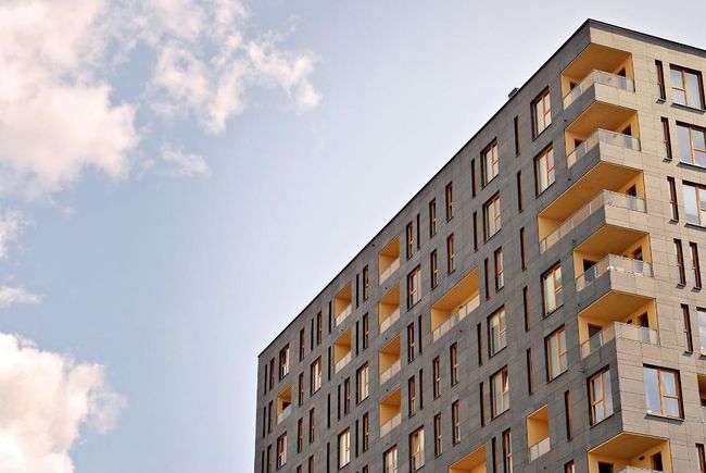 Edificio moderno de varias plantas con el cielo nublado como fondo. El edificio cuenta con balcones y ventanas rectangulares.