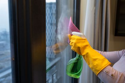 Eine Frau mit gelben Handschuhen putzt ein Fenster mit einer Sprühflasche.