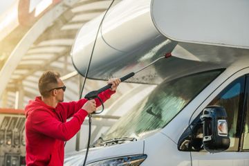 Ein Mann wäscht einen Wohnwagen mit einem Hochdruckreiniger.