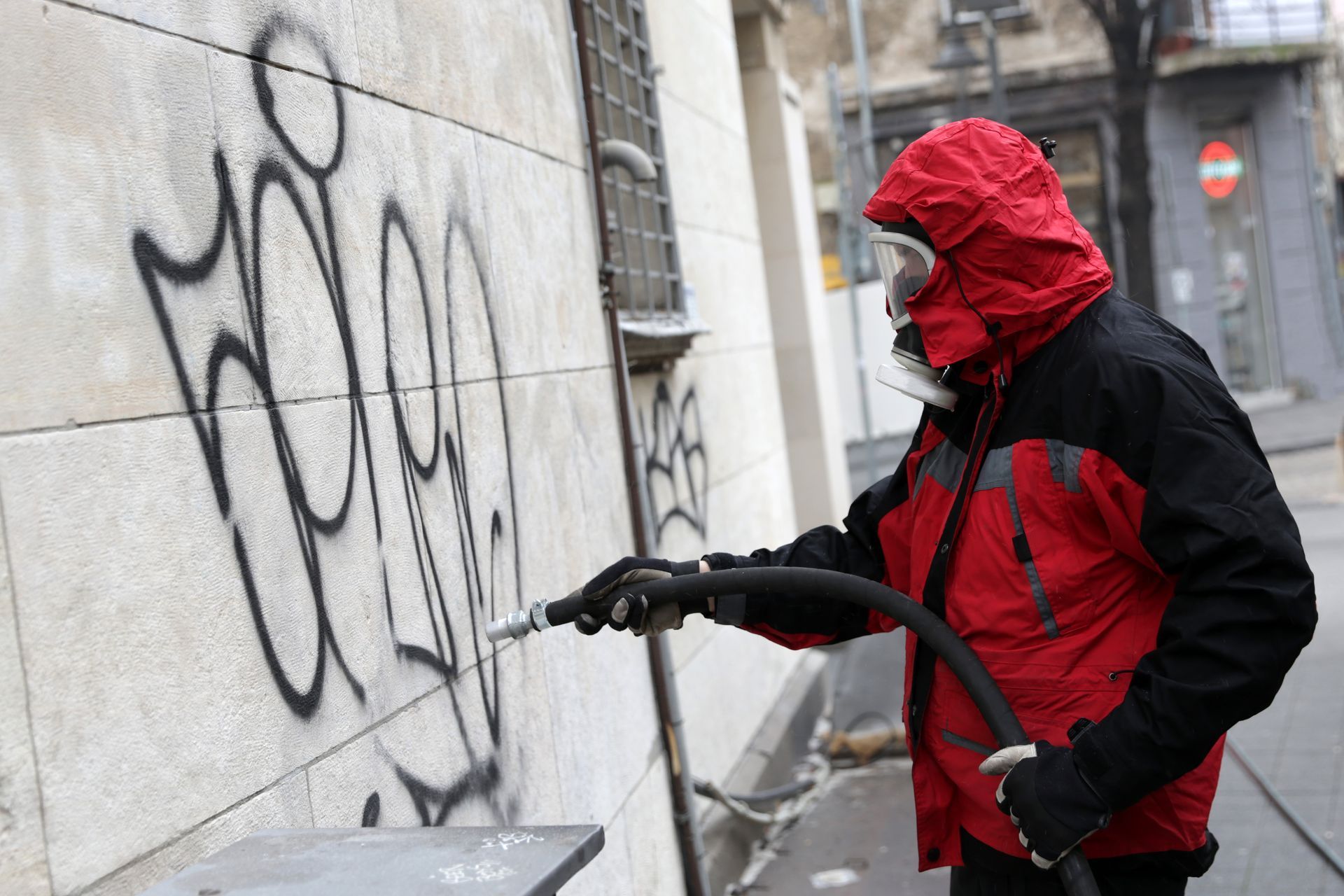 Ein Mann in einer roten Jacke entfernt Graffiti von einer Wand.