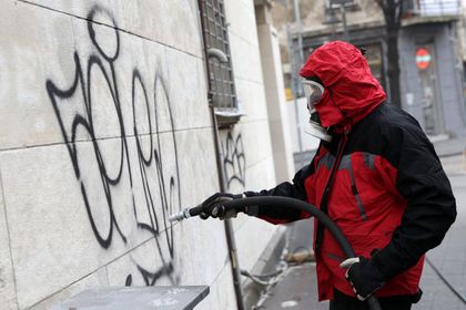 Ein Mann in einer roten Jacke entfernt Graffiti von einer Wand.