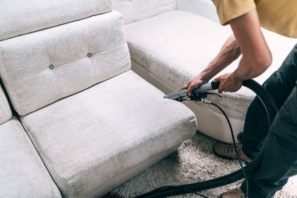 Ein Mann reinigt ein Sofa mit einem Staubsauger.