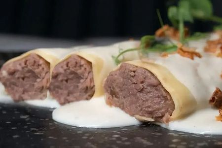 Rollitos de pasta rellenos servidos en un plato oscuro con salsa blanca cremosa y hierbas.