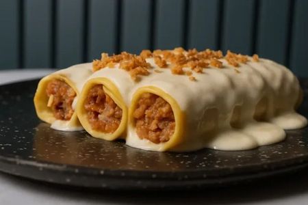 Enchiladas enrolladas cubiertas de crema y adornadas con migas de pan en un plato negro.