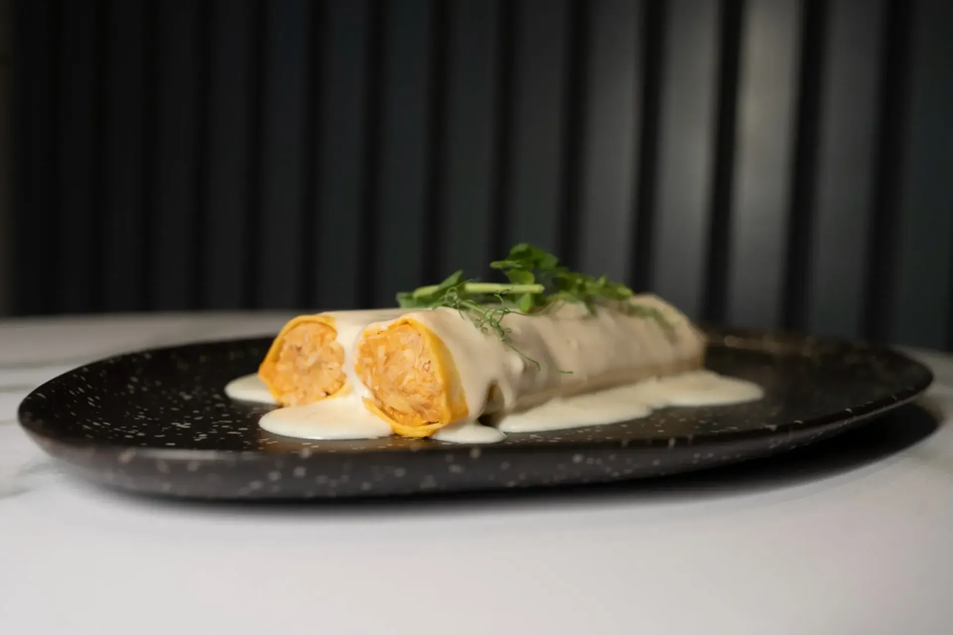 Enchiladas en plato moteado, cubiertas con salsa blanca, adornadas con hierbas.