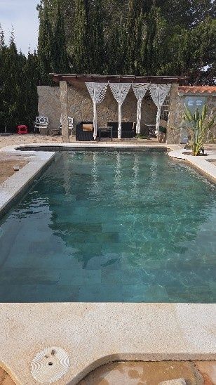 Piscina al aire libre con agua turquesa, situada junto a una cabaña con sombra y tumbonas, rodeada de árboles.