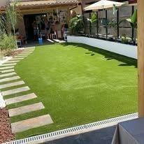 Pequeño patio trasero con césped artificial, losas para caminar y zona de estar a la sombra.