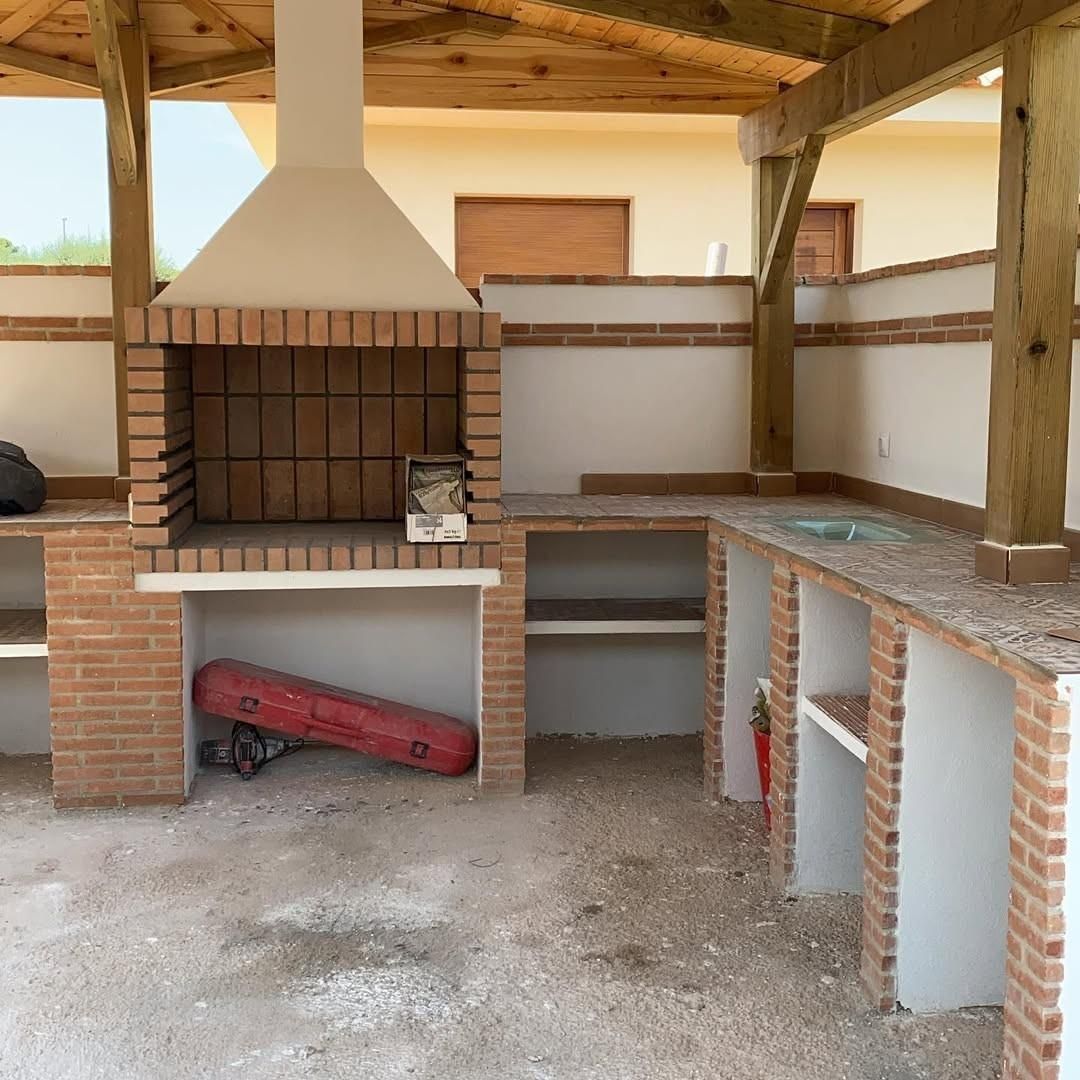 Zona de barbacoa exterior cubierta de ladrillo con chimenea, fregadero y encimera bajo un techo de madera.