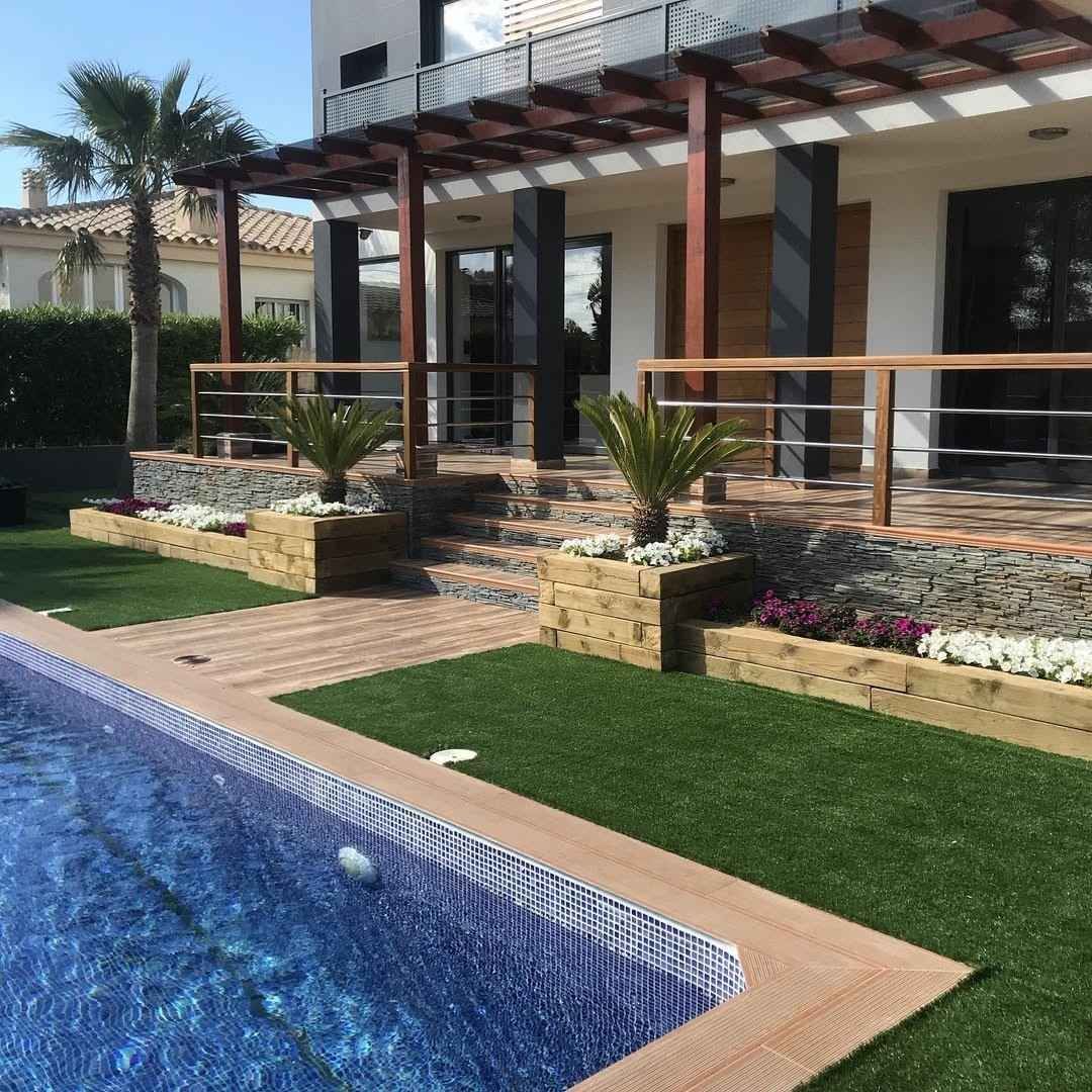 Patio de lujo junto a una piscina con azulejos azules, pérgola, barandillas y jardineras ajardinadas.