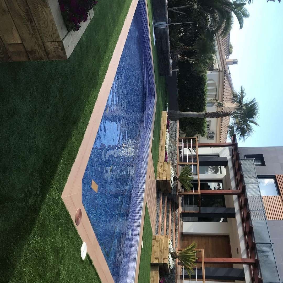 Patio trasero moderno con piscina de azulejos azules, césped, zona de estar en el patio y una casa contemporánea.