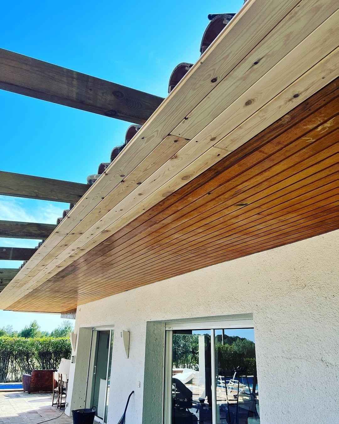 Exterior de una casa moderna con estuco blanco, techo de madera y vigas de techo a la vista bajo el cielo azul.