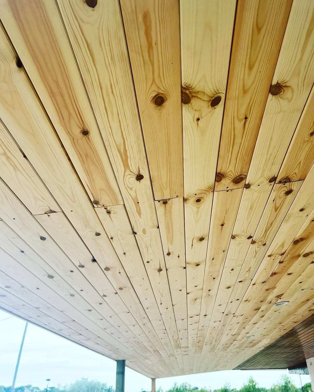 Techo de tablones de madera visto desde abajo, con un atisbo del cielo y postes de soporte en el borde.