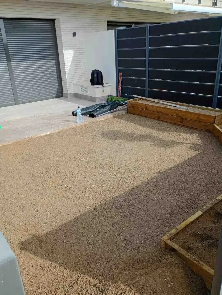 Patio delantero con acabado de guijarros, portón negro, puerta corredera y jardineras elevadas.