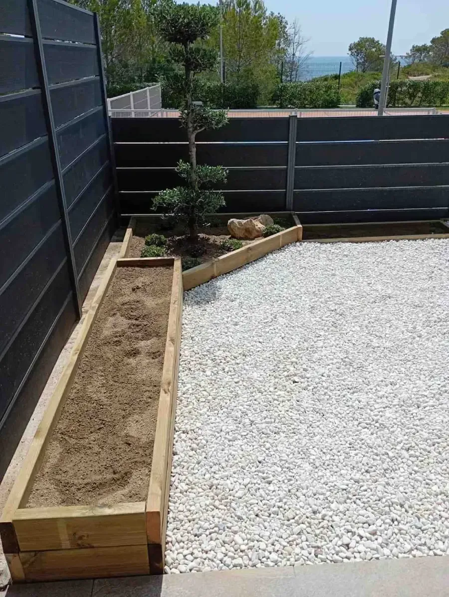 Pequeño patio trasero con terraza de grava, jardineras de madera elevadas y valla oscura que proporciona
