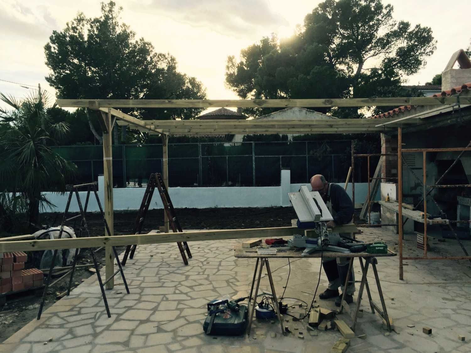 Obra en construcción al aire libre con trabajadores, andamios y herramientas frente a una estructura parcialmente construida.