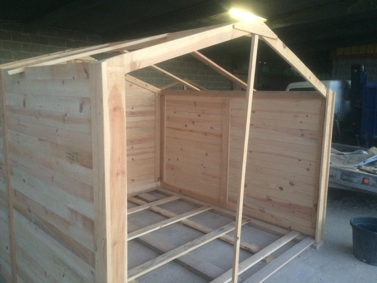 Estructura de cobertizo de madera parcialmente construida con techo y paneles laterales abiertos al anochecer.