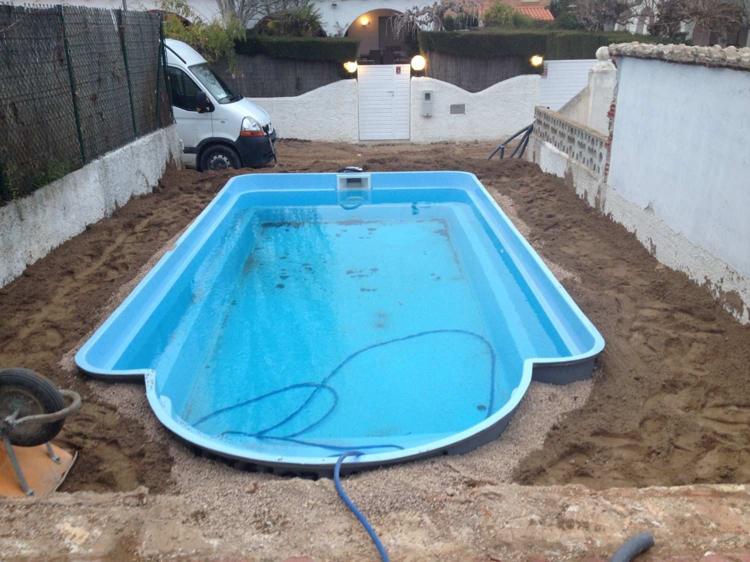 Piscina azul vacía en construcción, rodeada de tierra en un patio trasero.