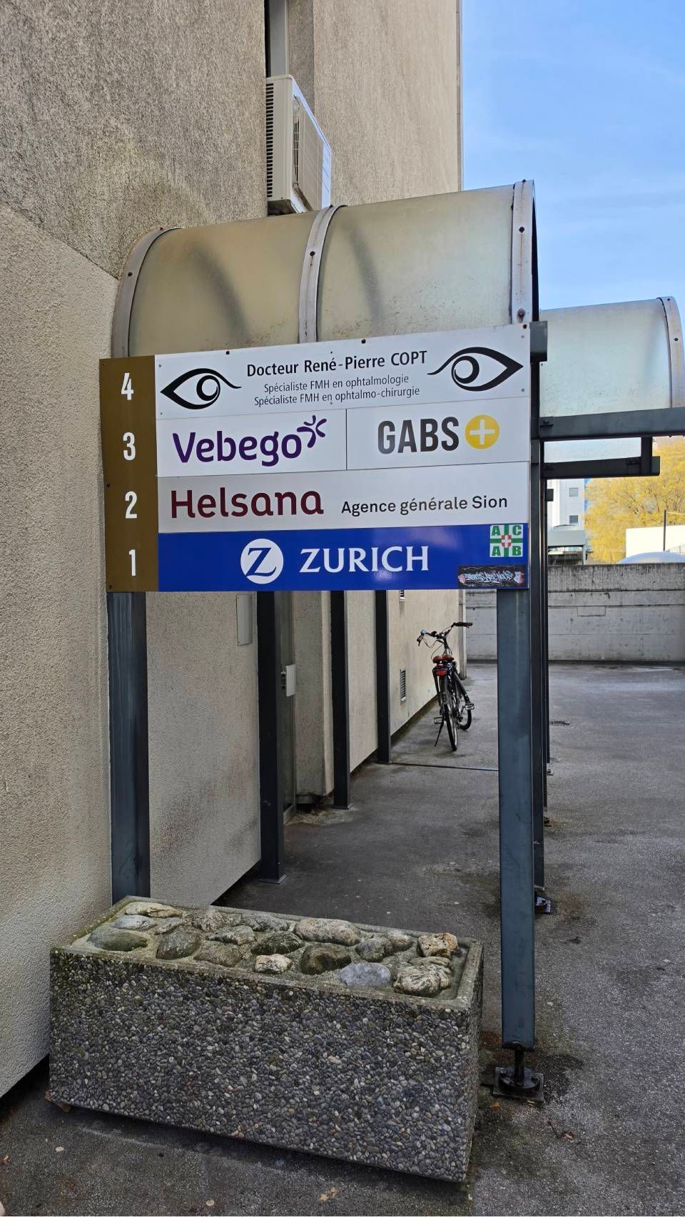 Panneaux indiquant Webegor, Helsana et Zurich sur le mur d'un bâtiment, dans une allée extérieure.