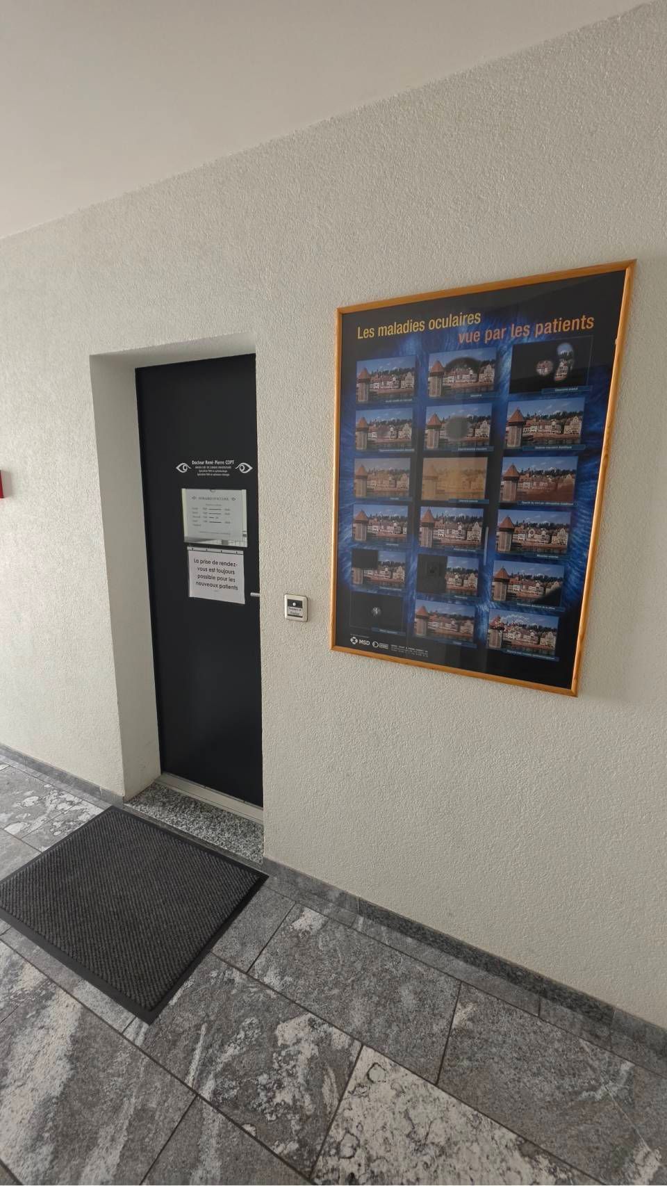 Entrée du bâtiment avec une porte sombre, un panneau d'affichage mural et une allée carrelée.